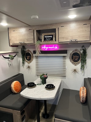 A compact kitchenette with a neon sign, a welcome sign, and decorative wall art.
