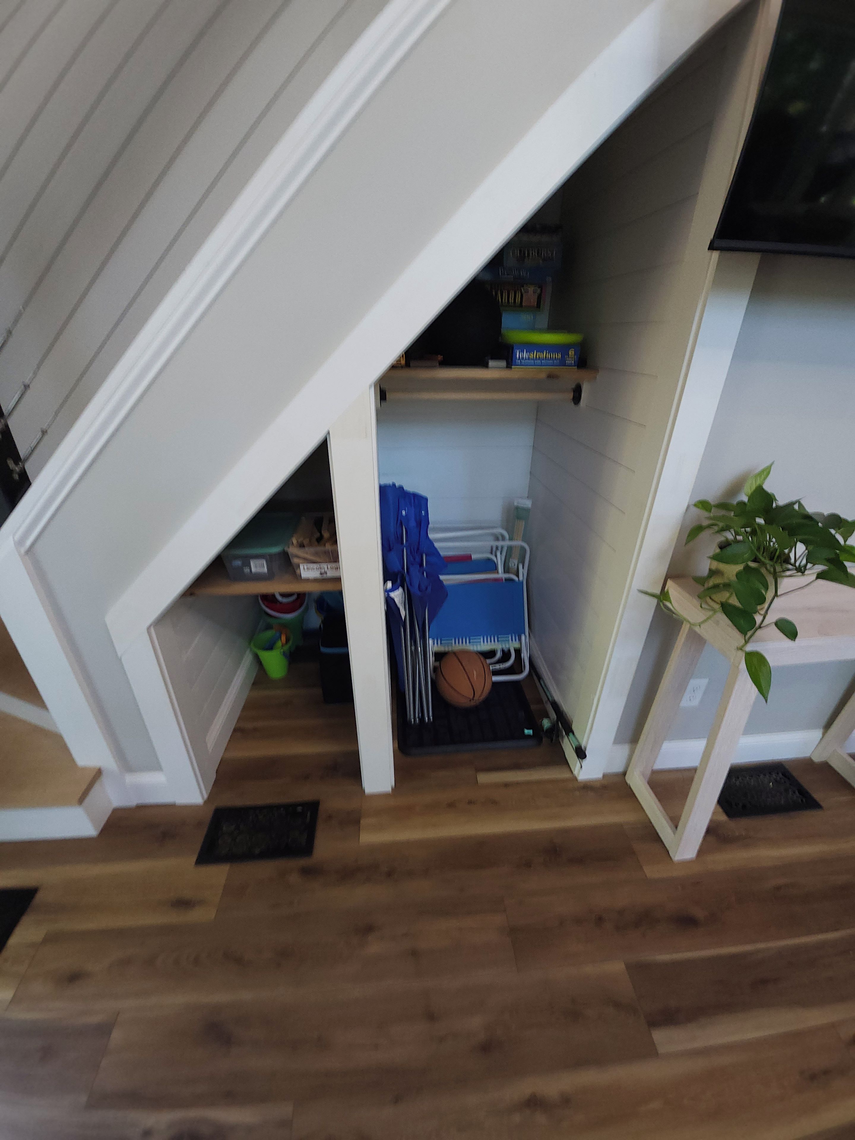 Une petite pièce mansardée avec un plafond en pente, une petite étagère remplie de livres, une chaise bleue et une plante en pot.