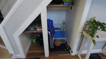 Une petite pièce mansardée avec un plafond en pente, une petite étagère remplie de livres, une chaise bleue et une plante en pot.