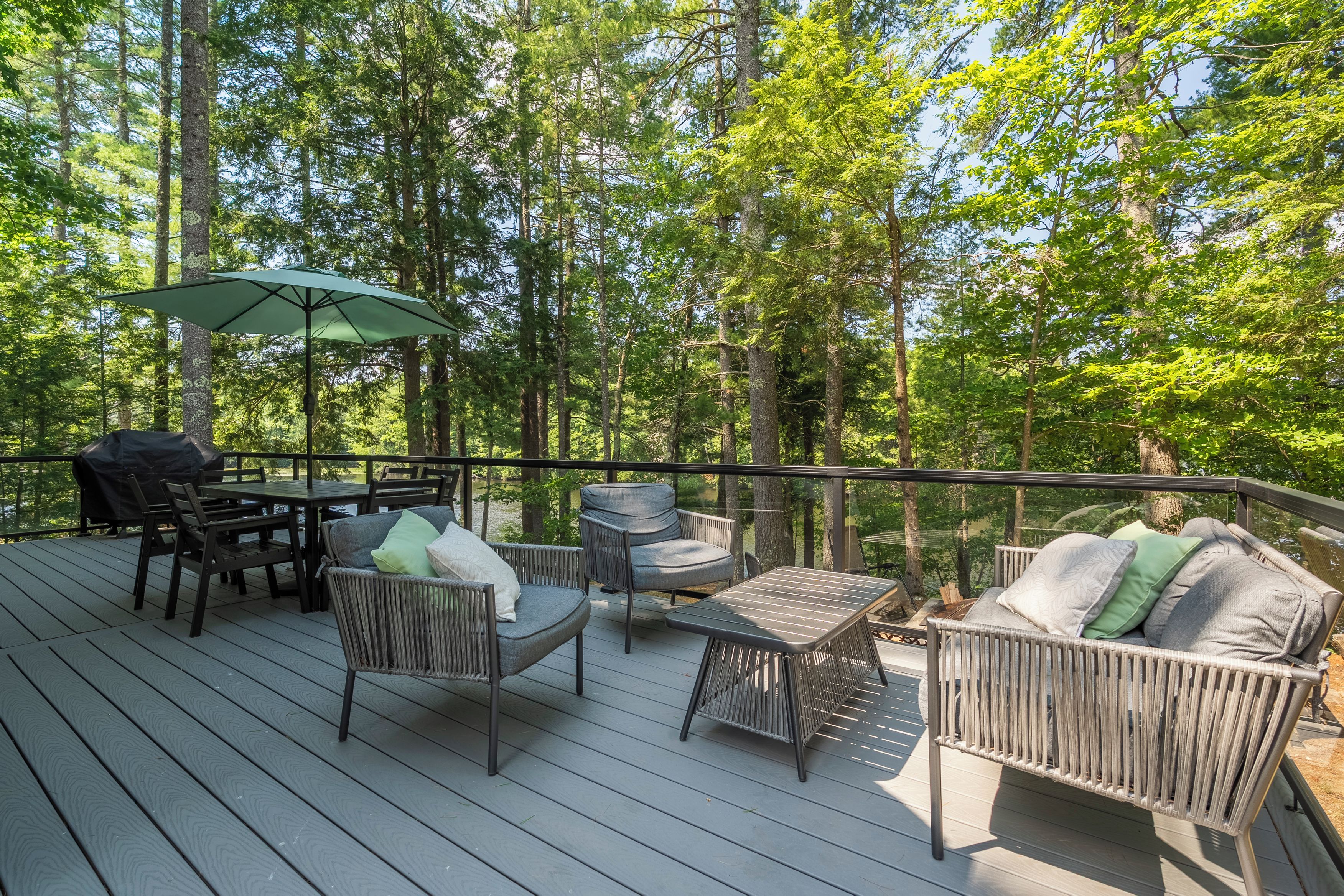 A deck with outdoor furniture, including chairs and a table, surrounded by trees.