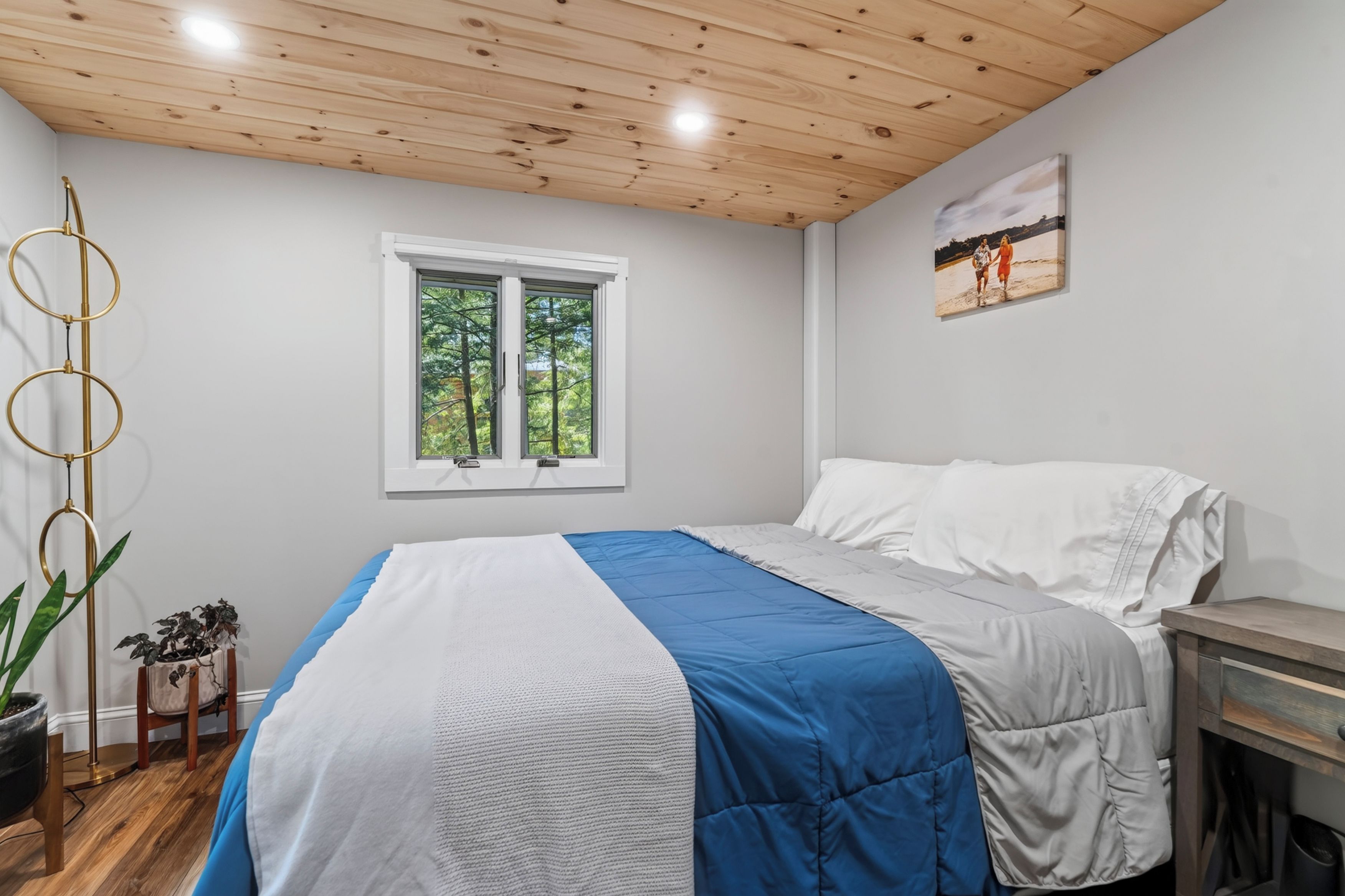 Une chambre à coucher avec un lit, une fenêtre, un tableau au mur et une plante.