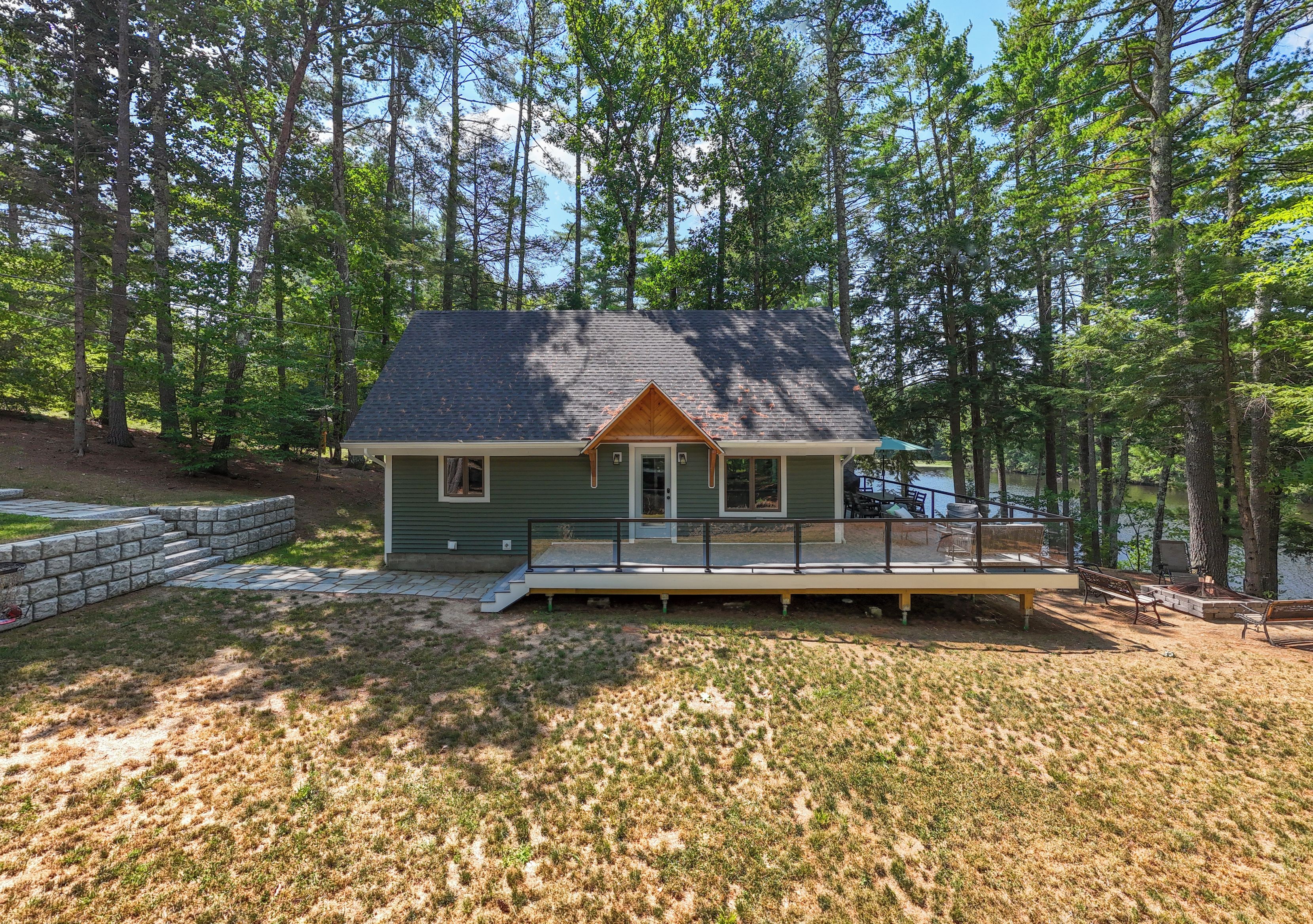 A single-story house with a porch, surrounded by a wooded area.