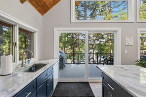 A modern kitchen with a large window, a sink, and a deck leading to a patio with outdoor furniture.
