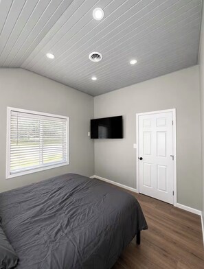 A bedroom with a bed, a mounted TV, a door, and a window with blinds. - Beautiful lake community home w hot tub (Andover)