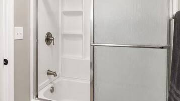 A walk-in shower with a glass door, a built-in shelf, and a shower control panel.