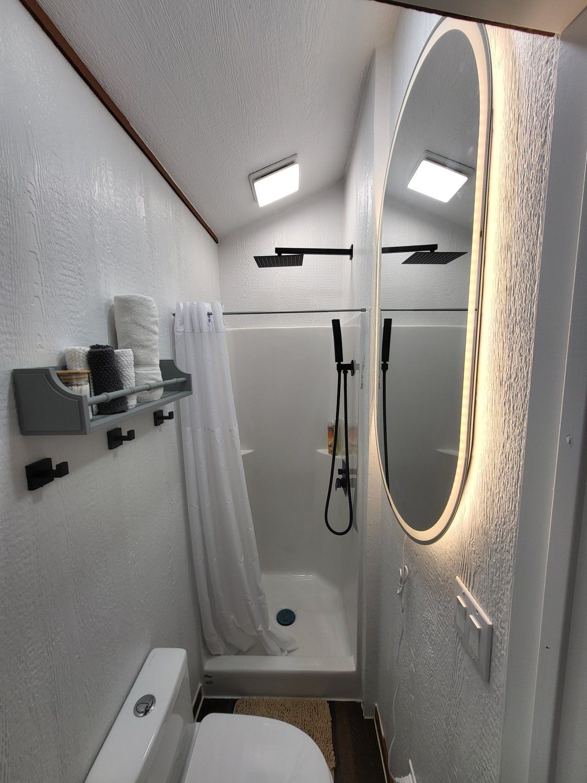 Ein kleines Badezimmer mit Dusche, Toilette und Spiegel.