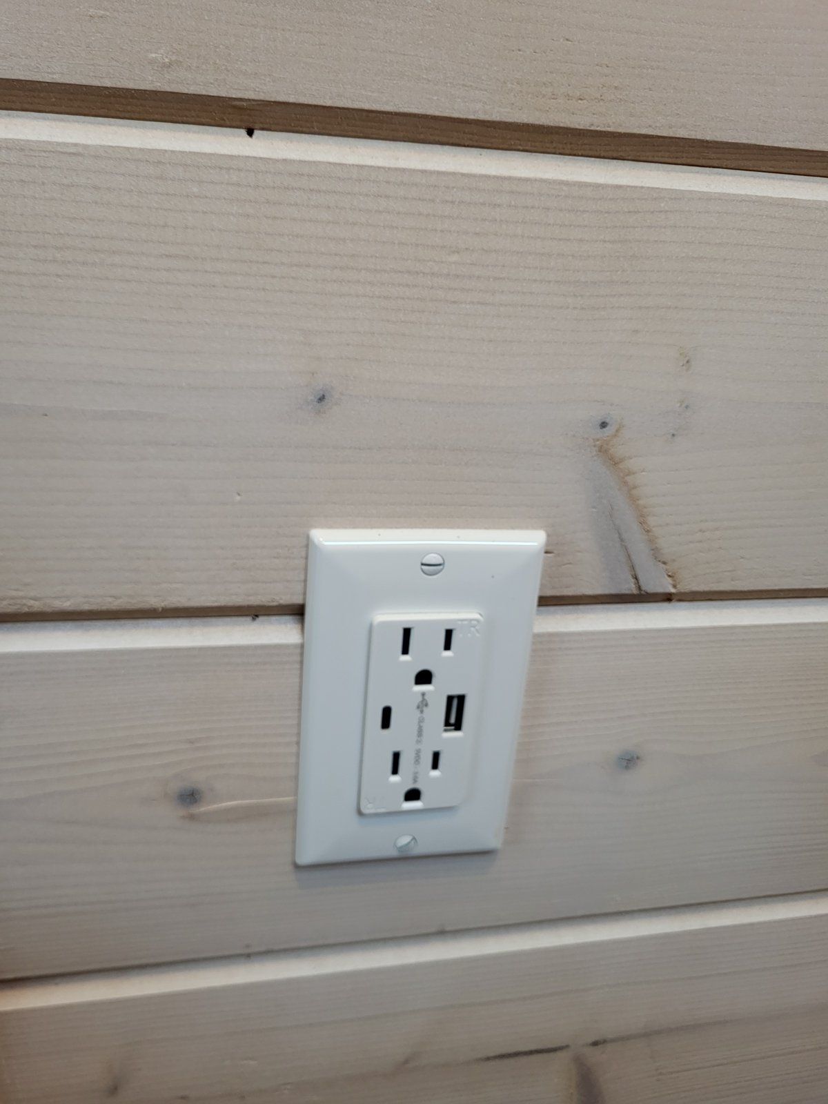 A white electrical outlet on a light-colored wooden wall.