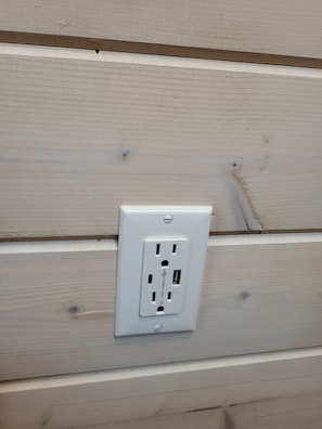 Eine weiße Steckdose an einer hellen Holzwand.