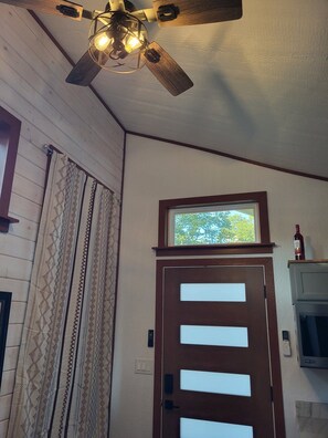 Ein Zimmer mit Deckenventilator aus Holz, einem Fenster mit Ausblick, einer Tür mit Fenster und einem an der Wand montierten Fernseher.