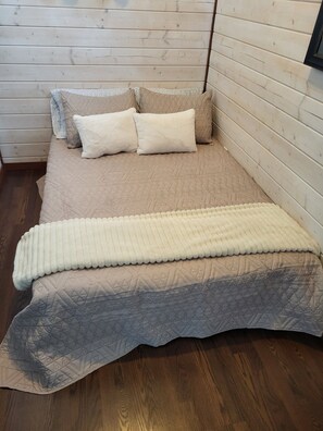 Ein Bett mit gesteppter Bettdecke und Kissen, Holzwände und ein Holzboden.