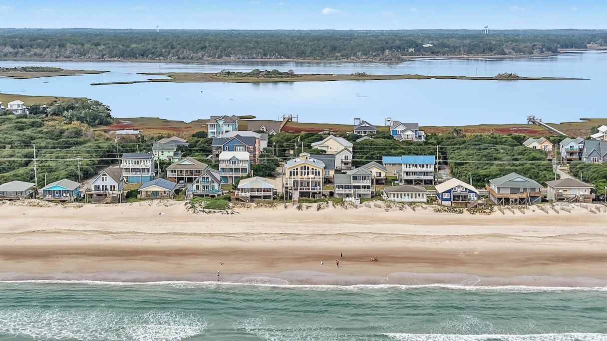 A coastal residential area with houses along the beach, a view of the sea, and a distant body of water.