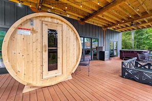 Una struttura sauna in legno con una porta, un patio con posti a sedere all'aperto e vista su una zona residenziale.