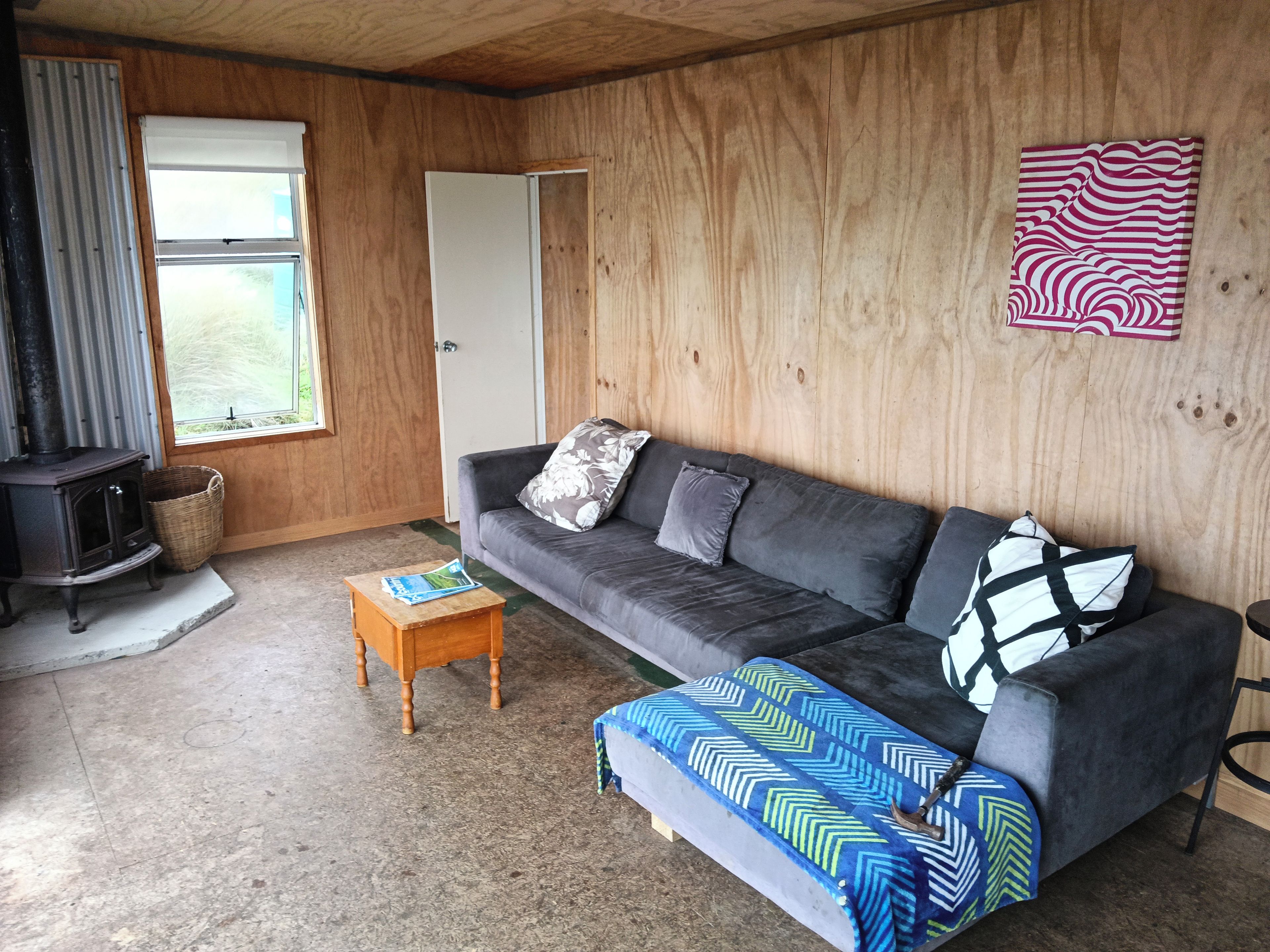 Un salon chaleureux avec un canapé, une petite table en bois, un plaid à motifs, une œuvre d’art accrochée au mur et un mur lambrissé.