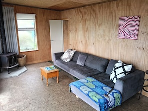 A cozy living room with a sofa, a small wooden table, a patterned throw blanket, a wall-mounted artwork, and a wood-paneled wall.