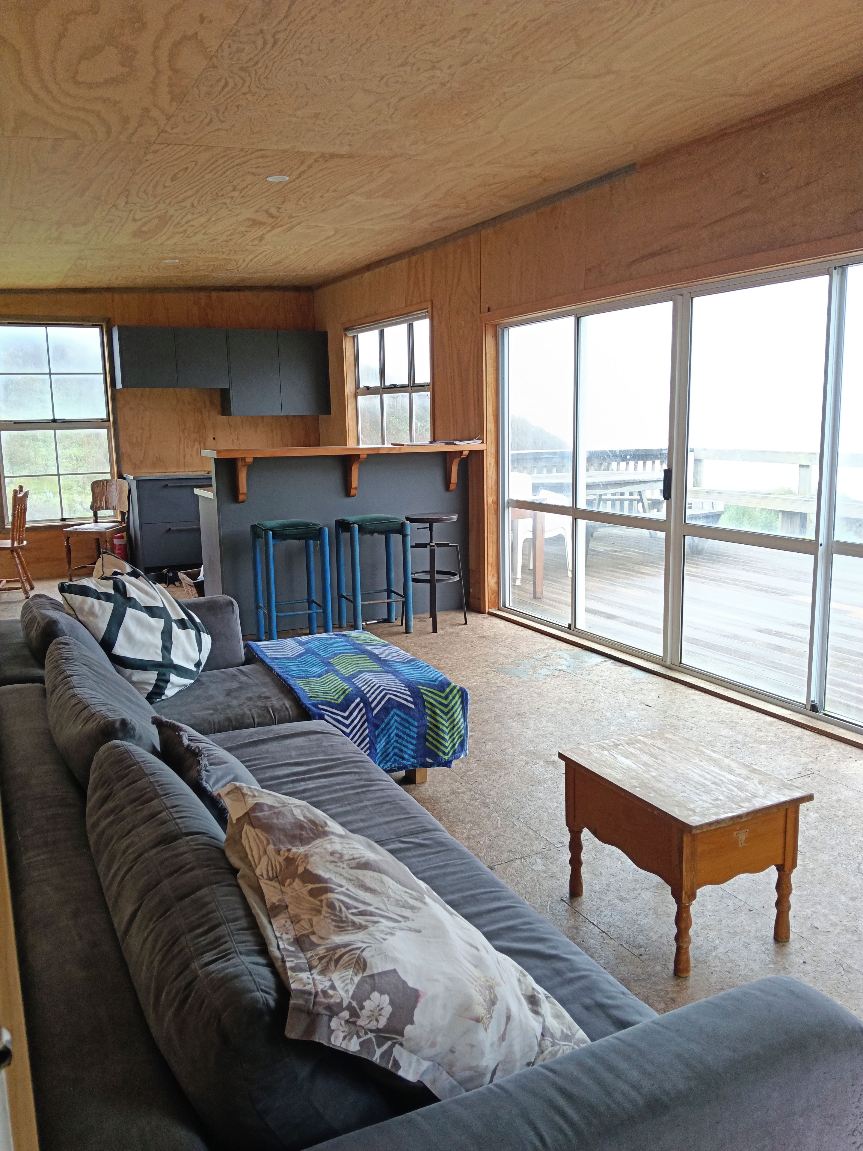 A spacious living area with a long sofa, a wooden coffee table, and a view through large windows.