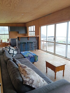 A spacious living area with a long sofa, a wooden coffee table, and a view through large windows.