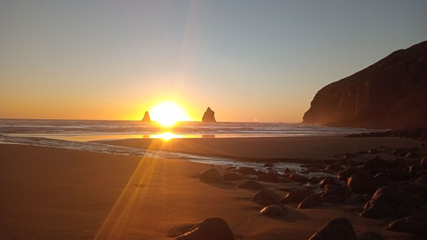 A beach with rocks and a cliff, and the sun is setting in the background.
