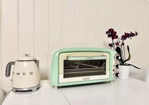 A vintage-style toaster oven and a kettle on a white surface, with a potted plant beside them.