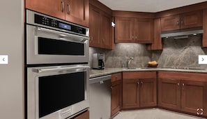 Une cuisine équipée d’appareils électroménagers en acier inoxydable, de meubles en bois et de plans de travail en granit.