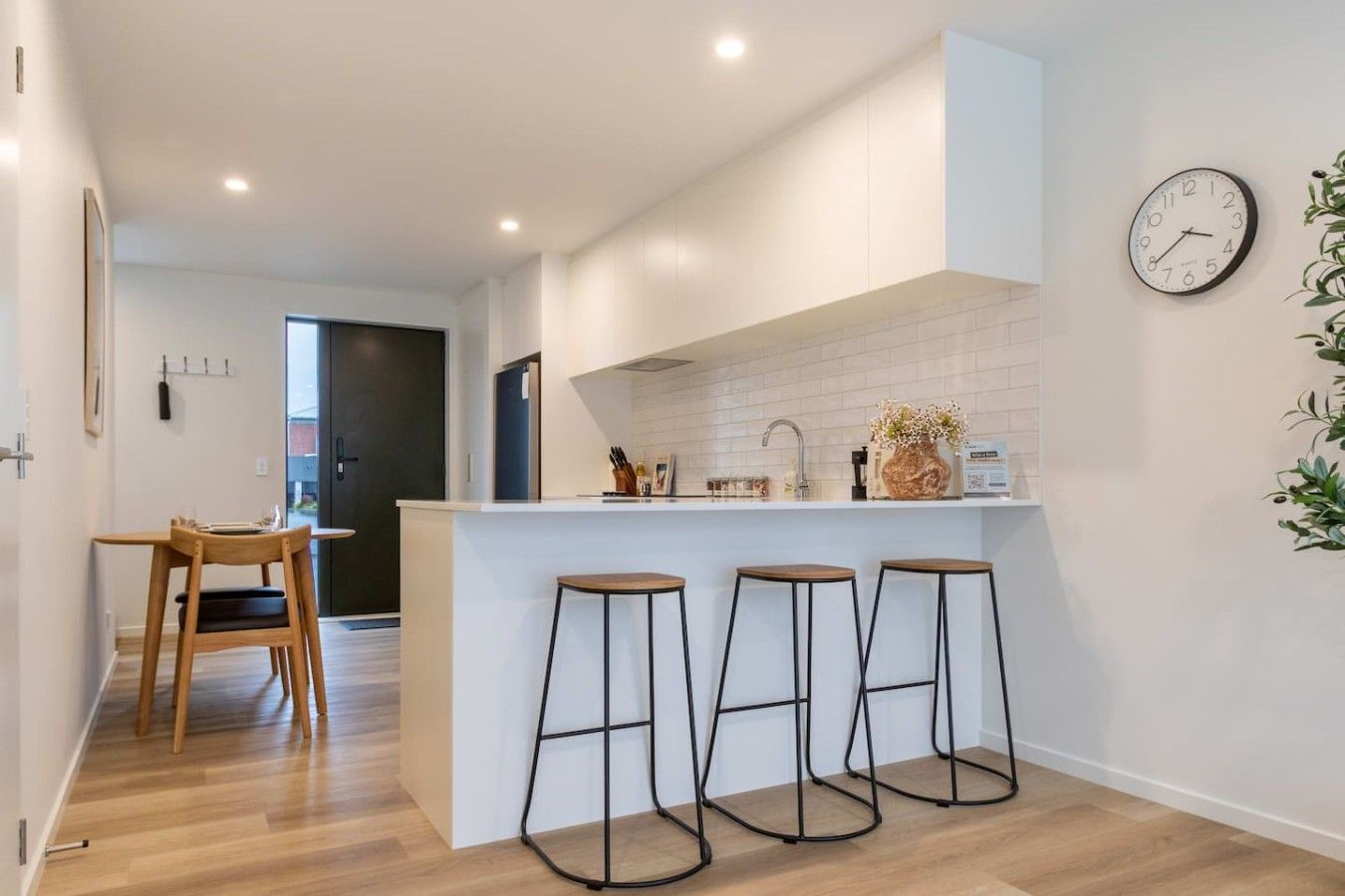 Una cocina moderna con una isla central, taburetes de bar, un reloj y una planta en maceta.