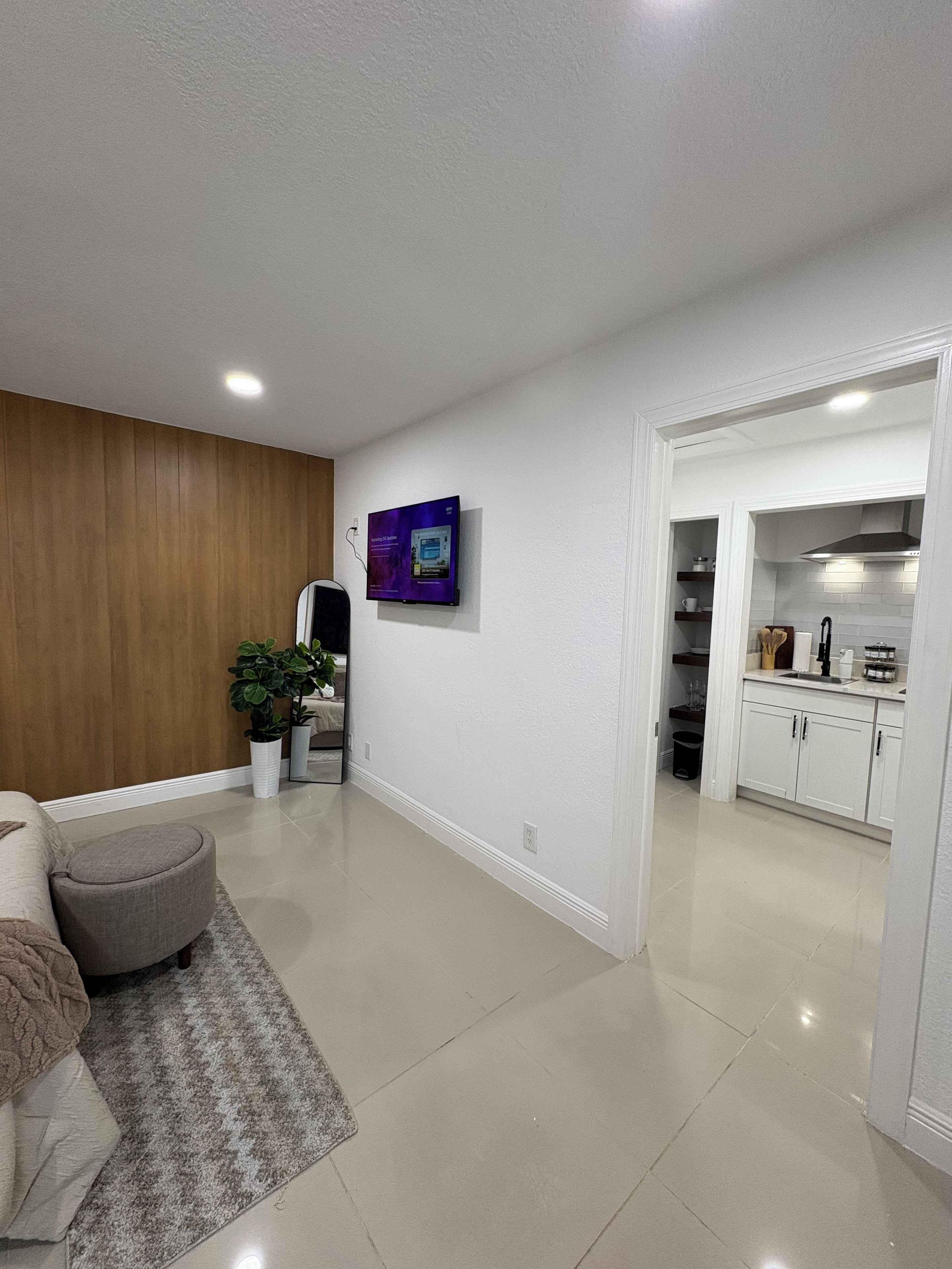 A modern living room with a flat-screen TV mounted on the wall, a wooden accent wall, a grey sofa, and a patterned rug.