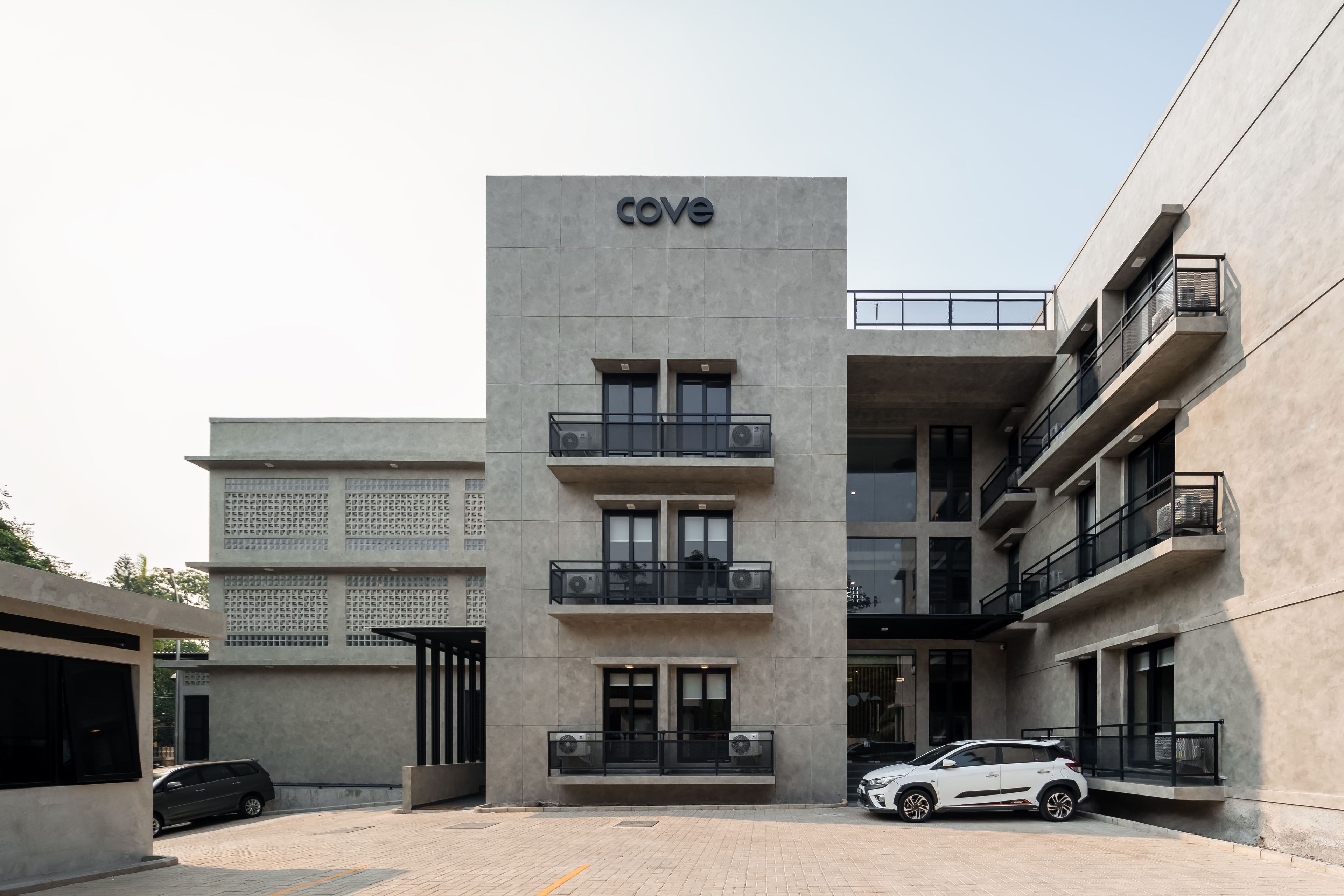 Ein modernes Gebäude mit einem 'COVE'-Schild, mehreren Balkonen und einem weißen Auto vor der Fassade.