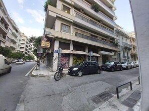 A multi-story building with balconies, parked cars, and a motorcycle on the sidewalk. - Athens Plaza Luxury Apartments (Athens)