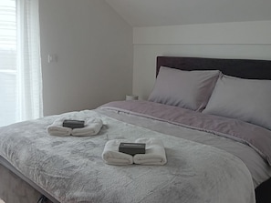 A neatly made bed with a headboard, pillows, and two folded towels with a welcome box on each. - Modern Holiday Home in Slavonia with Heated Pool, Spa and Private Pond (Nova Kapela)