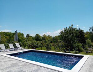 A rectangular swimming pool with a tiled deck, surrounded by greenery and trees. - Modern Holiday Home in Slavonia with Heated Pool, Spa and Private Pond (Nova Kapela)