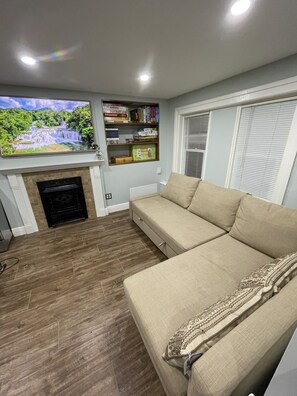 Una sala de estar con un sofá beige, una chimenea, una estantería y un ventanal grande.