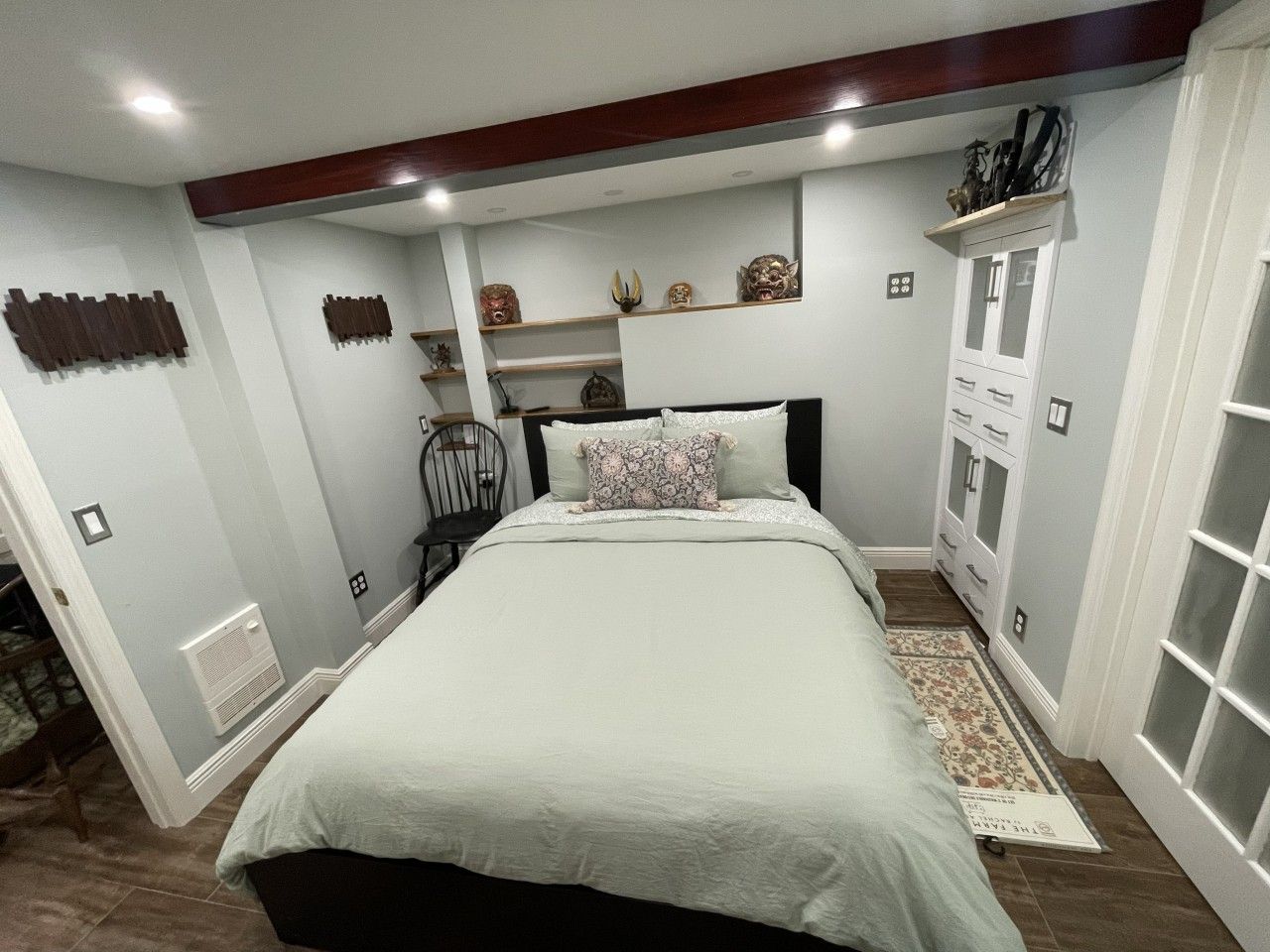 Un dormitorio con cama, mesita de noche, silla, cómoda y objetos decorativos en estanterías.