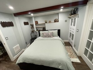 Un dormitorio con cama, mesita de noche, silla, cómoda y objetos decorativos en estanterías.