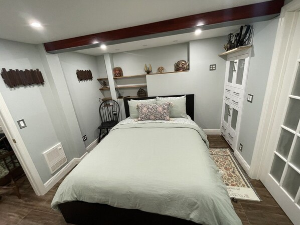A bedroom with a bed, a nightstand, a chair, a dresser, and decorative items on shelves. - Upscale downtown Garden Level 2BR, Full Kitchen (Albany)