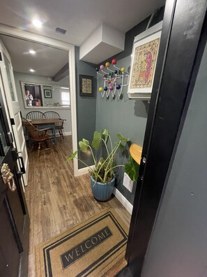 A hallway with a welcome mat, a potted plant, a wall-mounted rack with colorful balls, and a framed picture. - Upscale downtown Garden Level 2BR, Full Kitchen (Albany)