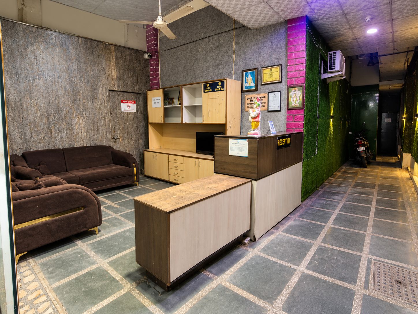 Un espace d’accueil comprenant un canapé, un comptoir de réception et un mur végétal orné d’une fresque.