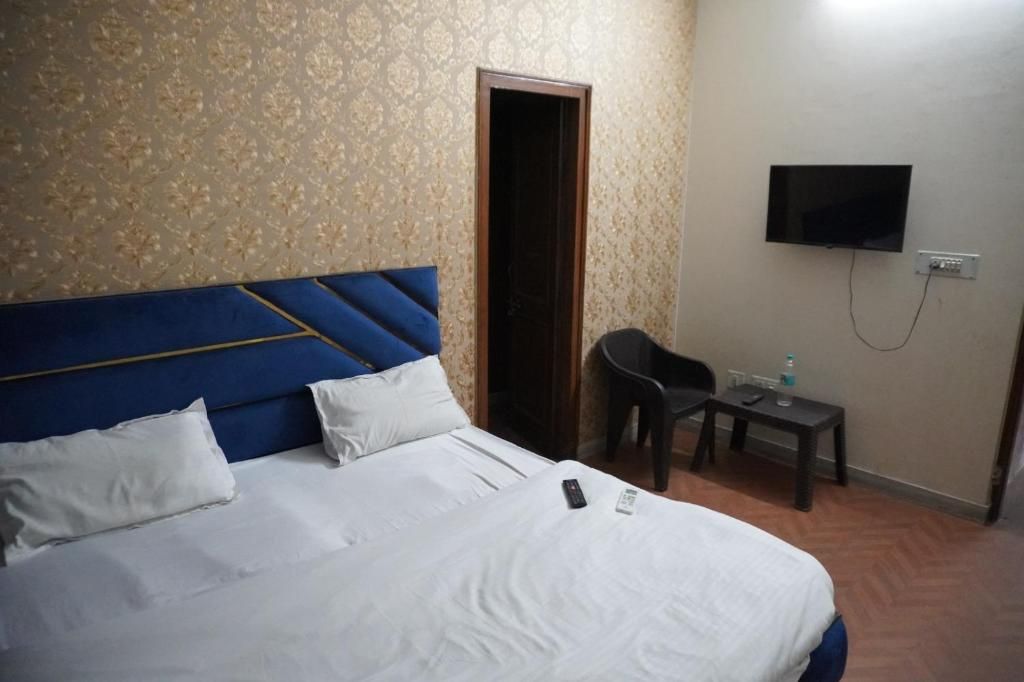 Une chambre d’hôtel avec un lit, un téléviseur fixé au mur, une petite table avec une chaise et une porte.