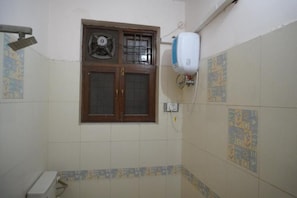 Un baño con un ventilador, un secador de manos y una ventana con diseño de celosía.