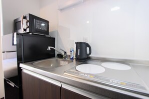 Una cocina compacta con microondas, hervidor y pileta.