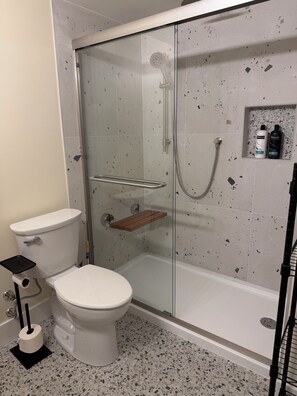 Ett badrum med en dusch som är avskärmad med glasväggar, en toalett och en hylla med toalettartiklar.