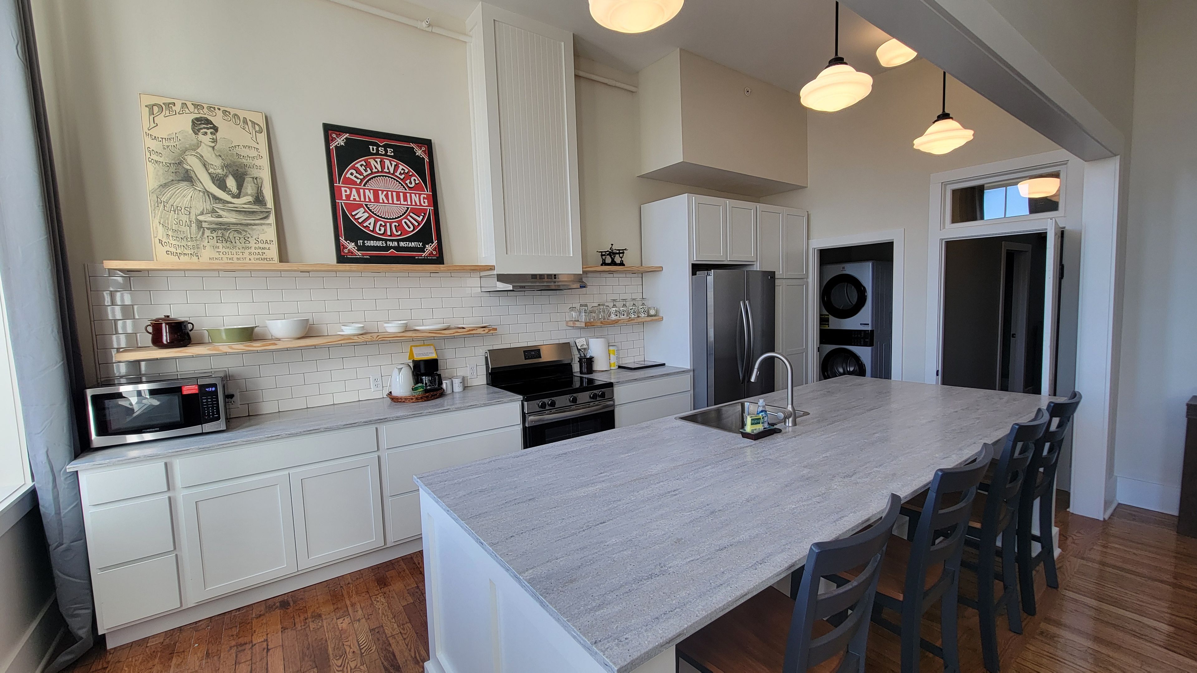 A modern kitchen with white cabinetry, a central island, stainless steel appliances, and pendant lighting.