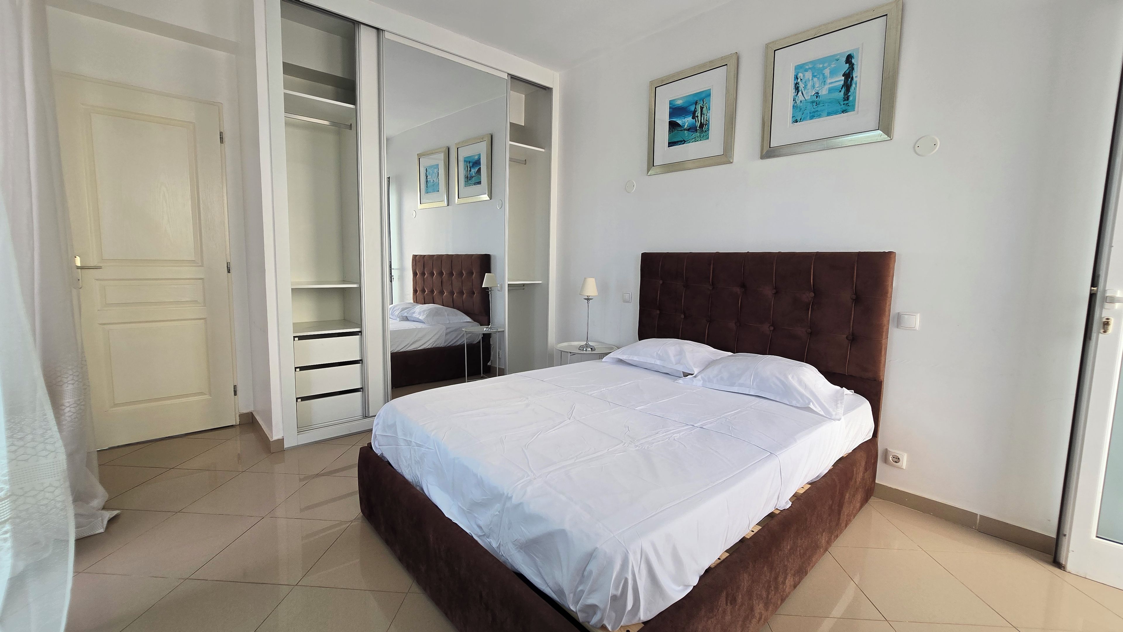 Un dormitorio con una cama, un armario y dos cuadros en la pared.