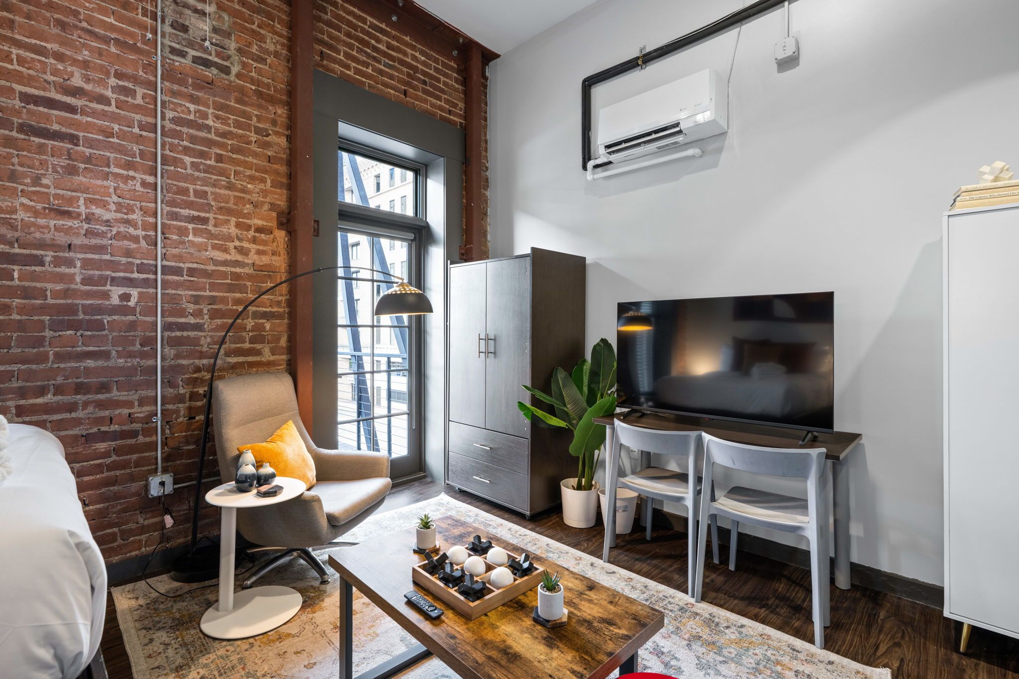 A modern living room with a brick wall, a large window, a flat-screen TV, a sofa, a coffee table, and a cabinet.