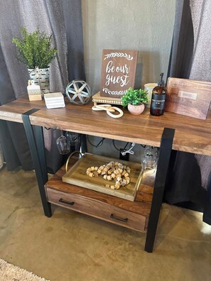 A wooden table with a sign that reads 'be our guest,' a bottle of hand sanitizer, and a tray with wooden blocks. - Cozy 2-bedroom house in Idabel, OK only 10 miles to Broken Bow, OK (Idabel)
