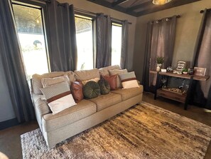 A living room with a sofa, a rug, and a shelf with various items. - Cozy 2-bedroom house in Idabel, OK only 10 miles to Broken Bow, OK (Idabel)