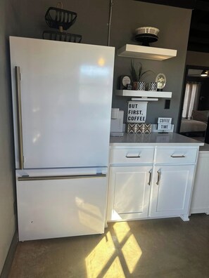A kitchen with a white refrigerator, a coffee bar sign, and a sign that says 'BUT FIRST, COFFEE TIME'. - Cozy 2-bedroom house in Idabel, OK only 10 miles to Broken Bow, OK (Idabel)