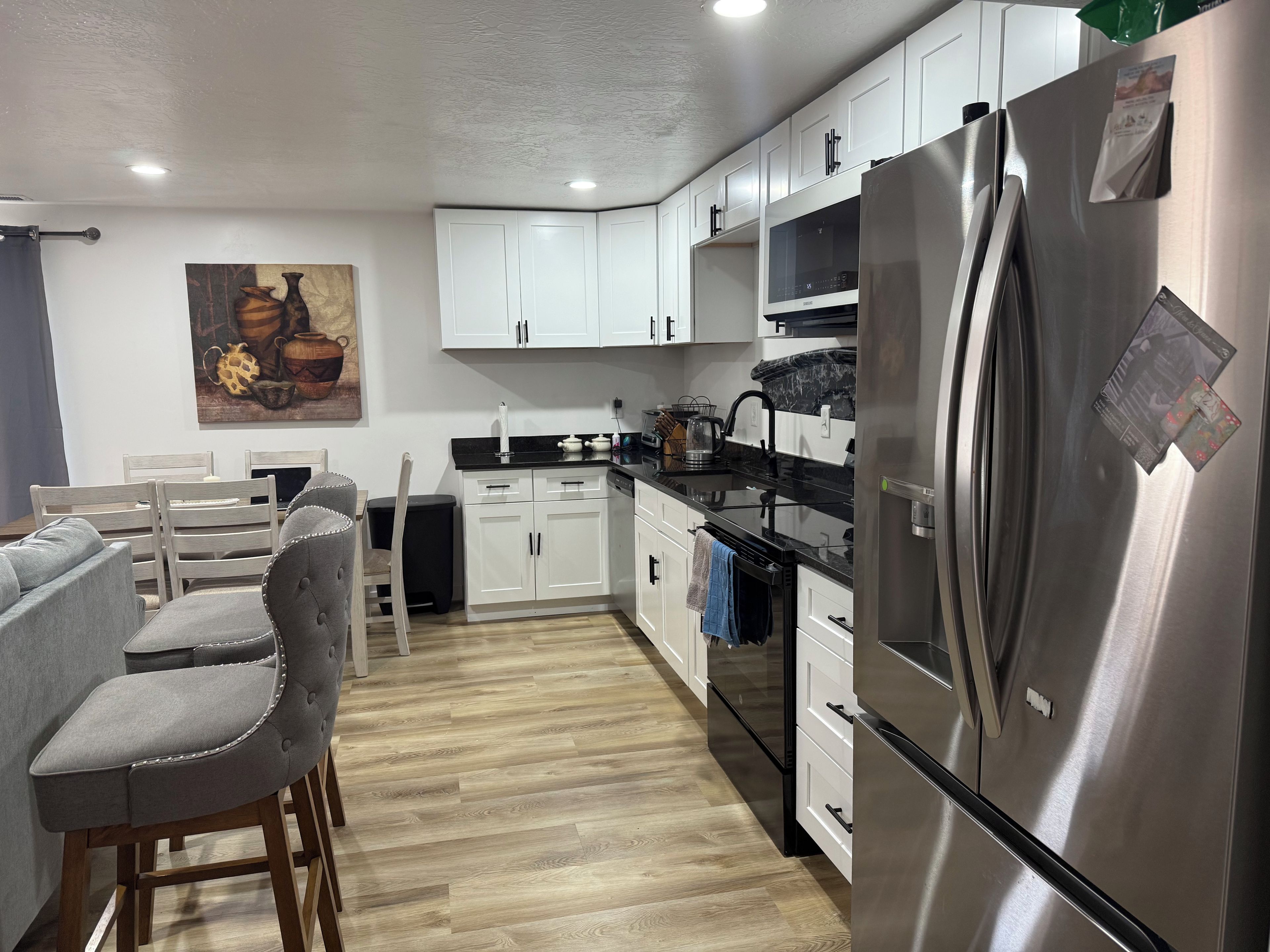 Una cocina moderna con armarios blancos, un refrigerador de acero inoxidable y un comedor con sillas tapizadas en gris.