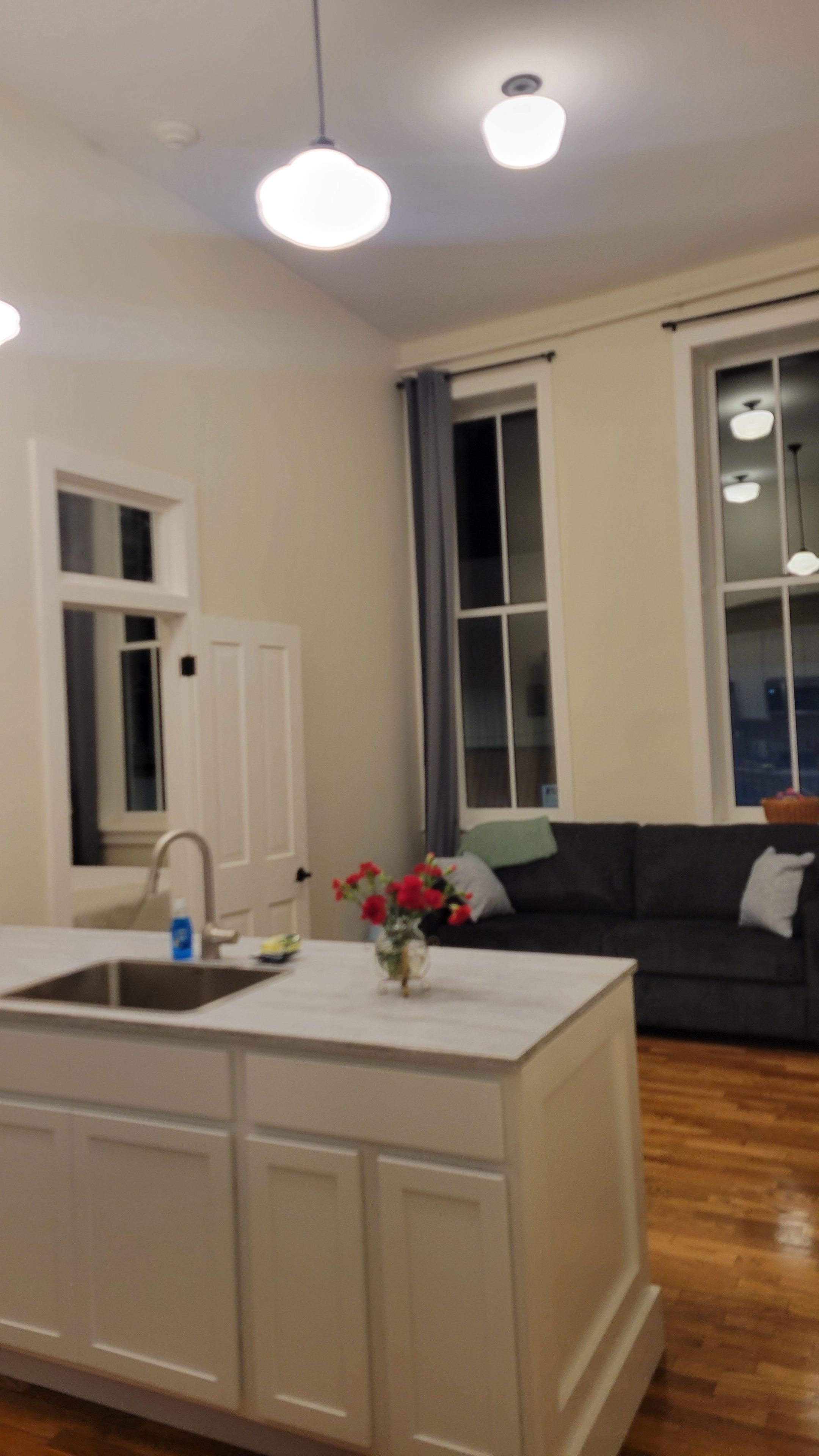 Eine Küche mit Kochinsel, ein Essbereich mit dunkelgrauem Sofa und ein großes Fenster mit Vorhängen.