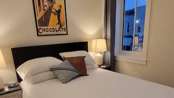 Una habitación de hotel con una cama, mesitas de noche, una lámpara, un cartel y una ventana con vistas.