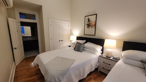 Une chambre d’hôtel comprenant un lit, des tables de chevet, une lampe fixée au mur, un tableau encadré et une porte donnant accès à une salle de bain.