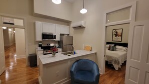 A compact kitchen with modern appliances, a small dining area, and a bedroom with a bed and a nightstand.